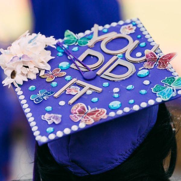 purple graduation cap decorated with flowers, butterflies, gems, and the words "you did it"