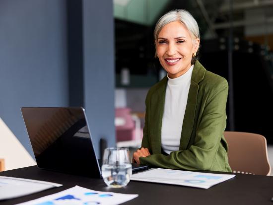 Professional-looking mature woman looking at camera with her laptop open in front of her.