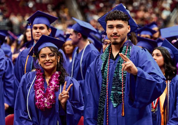 two students at graduation showing peace signs