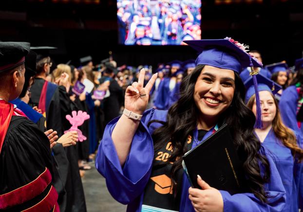student at graduation holding diploma and showing peace sign